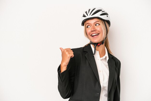 Young caucasian business woman wearing a bike helmet isolated on white background points with thumb finger away, laughing and carefree.