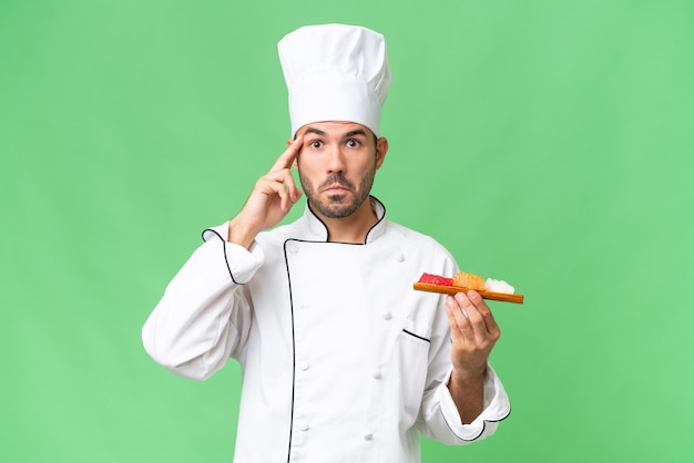 Young caucasian chef holding a sushi over isolated background thinking an idea