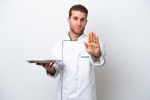 Young caucasian chef with tray isolated on white background making stop gesture