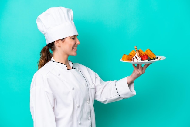 Young caucasian chef woman holding waffles isolated on blue background with happy expression