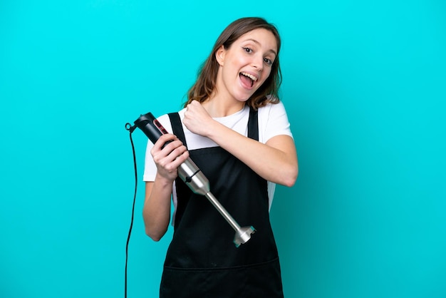 Young caucasian cooker woman using hand blender isolated on blue background celebrating a victory