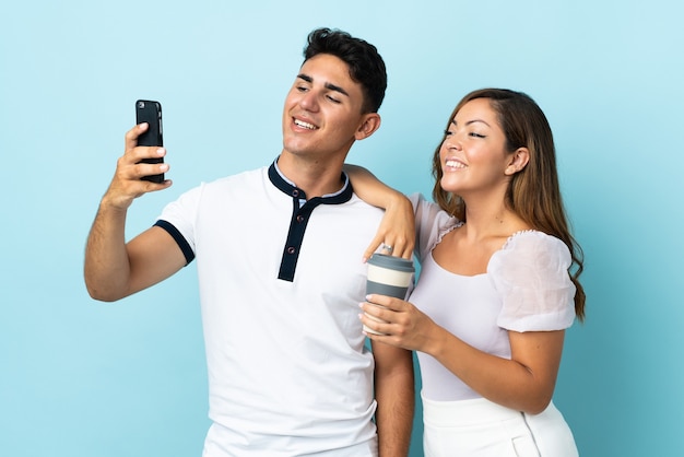 Young caucasian couple on blue making a selfie with the mobile