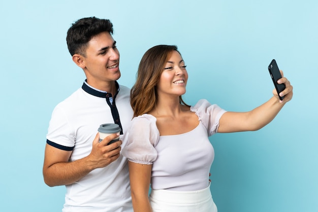 Young caucasian couple on blue making a selfie with the mobile