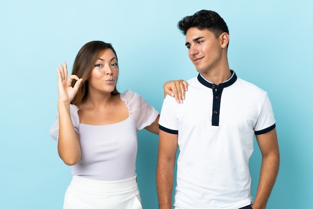 Young caucasian couple on blue showing an ok sign with fingers