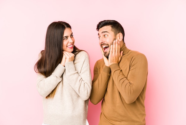 Young caucasian couple isolated keeps hands under chin, is looking happily aside.