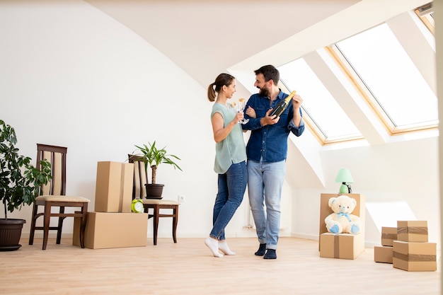 young caucasian couple opening champagne bottle to celebrate moving into new home