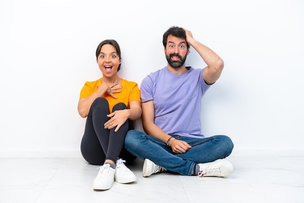 Young caucasian couple sitting on the floor isolated on white background with surprise facial expression