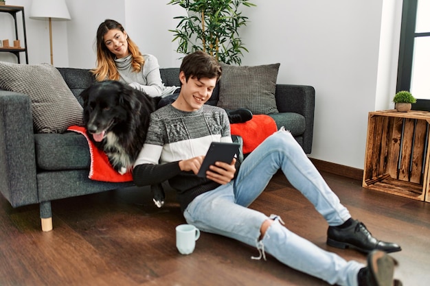 Young caucasian couple smiling happy with dog using touchpad at home