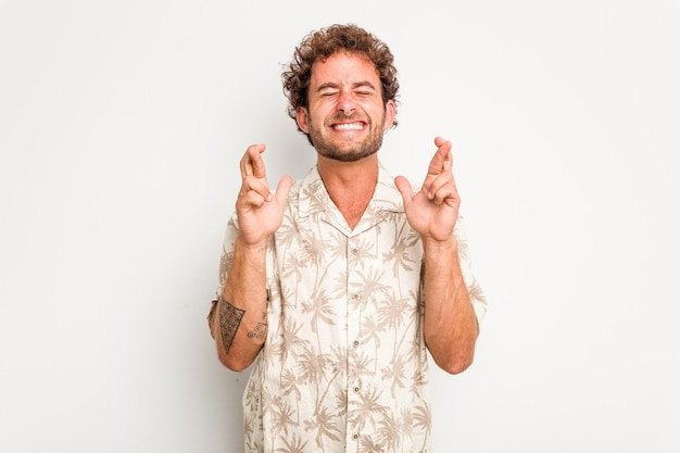 Photo young caucasian curly hair man isolated on white background crossing fingers for having luck