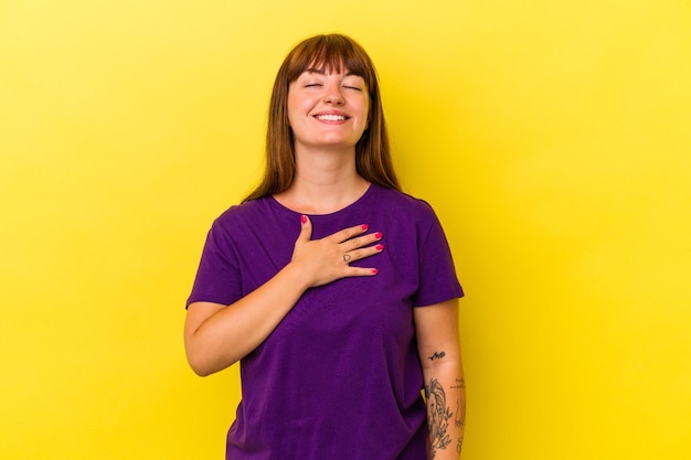 Young caucasian curvy woman isolated on yellow background laughs out loudly keeping hand on chest.