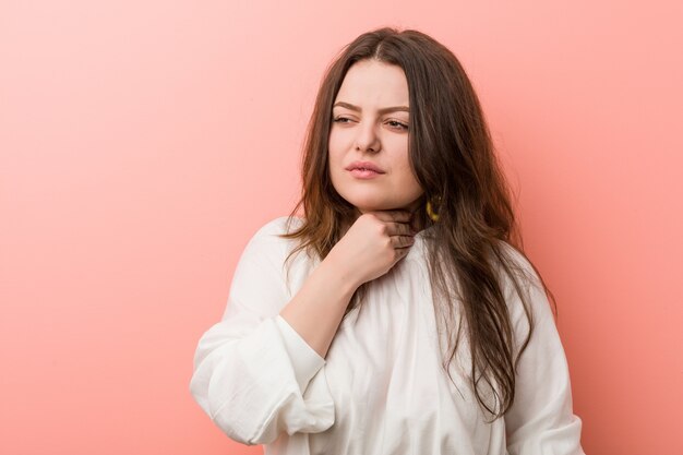 Young caucasian curvy woman standing against pink wall