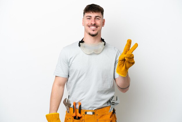 Young caucasian electrician man isolated on white background smiling and showing victory sign