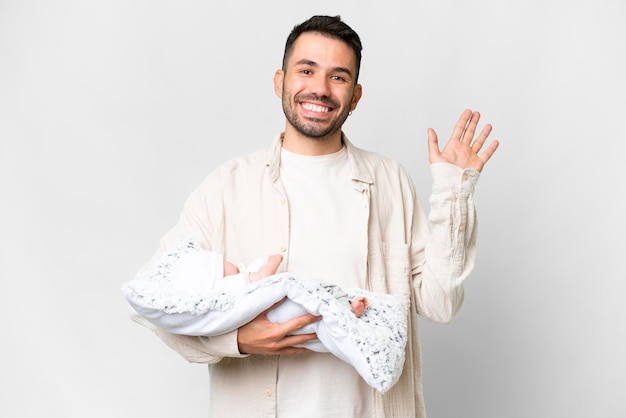 Young caucasian father with her newborn baby over isolated background saluting with hand with happy expression