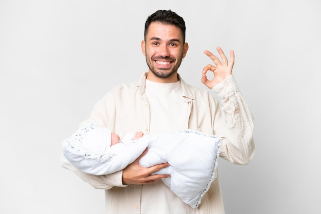 Young caucasian father with her newborn baby over isolated background showing ok sign with fingers