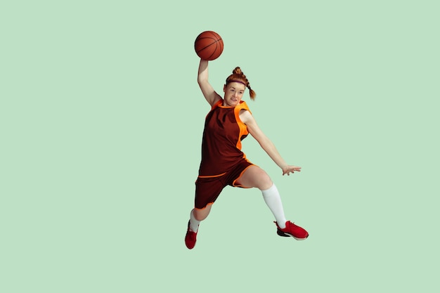 Young caucasian female basketball player in action motion in high jump isolated on mint