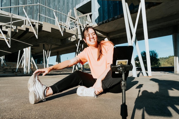 Young Caucasian female blogger recording video of fitness training using smartphone on tripod Sport and healthy life style on social network content Connect with the audience