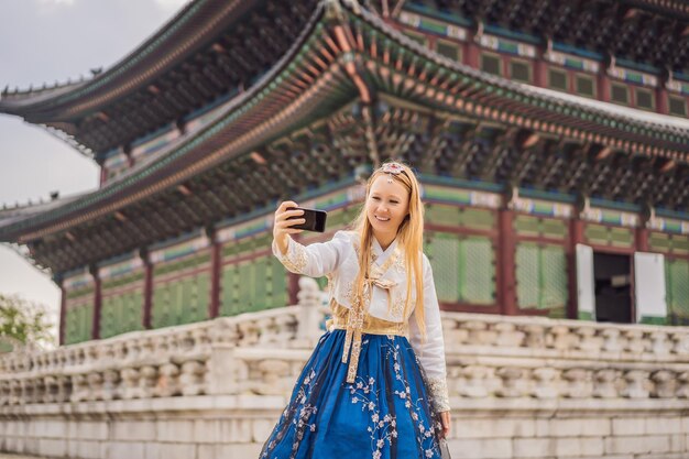 Photo young caucasian female tourist in hanbok national korean dress at korean palace travel to korea concept national korean clothing entertainment for tourists trying on national korean clothing