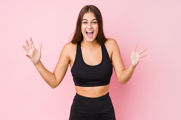 Young caucasian fitness woman doing sport receiving a pleasant surprise, excited and raising hands.