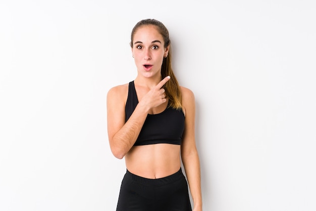 Young caucasian fitness woman posing in a white pointing to the side