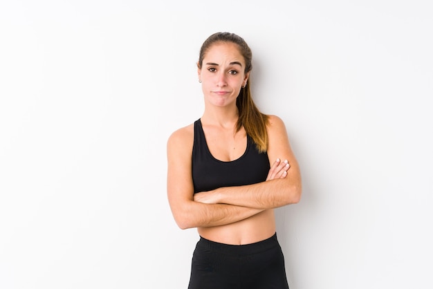 Young caucasian fitness woman posing in a white space unhappy looking in camera with sarcastic expression.