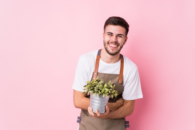 Photo young caucasian gardener man holding a plant isolated laughing and having fun.