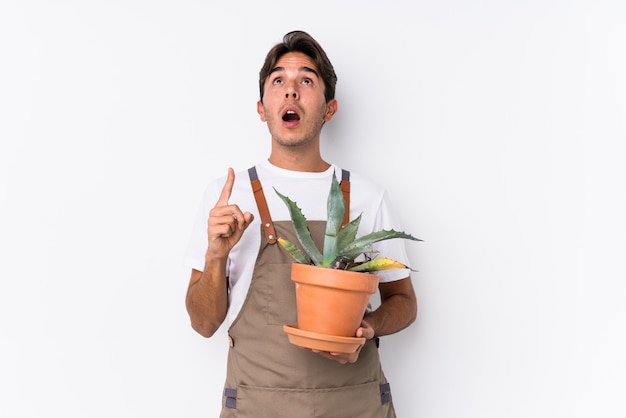 Young caucasian gardener man holding a plant isolated pointing upside with opened mouth.