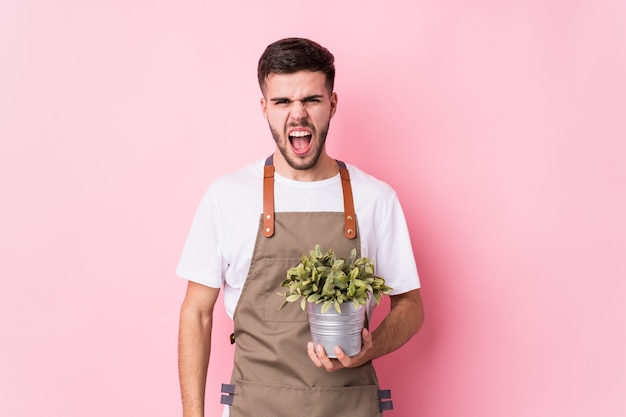 Photo young caucasian gardener man holding a plant isolated screaming very angry and aggressive.