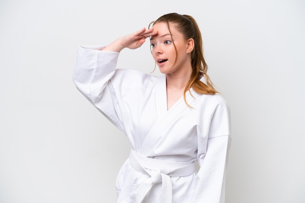 Young caucasian girl doing karate isolated on white background doing surprise gesture while looking to the side