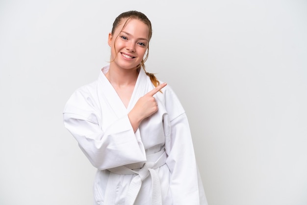 Young caucasian girl doing karate isolated on white background pointing to the side to present a product