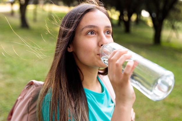 Young caucasian girl drinking water from a glass bottle at the park