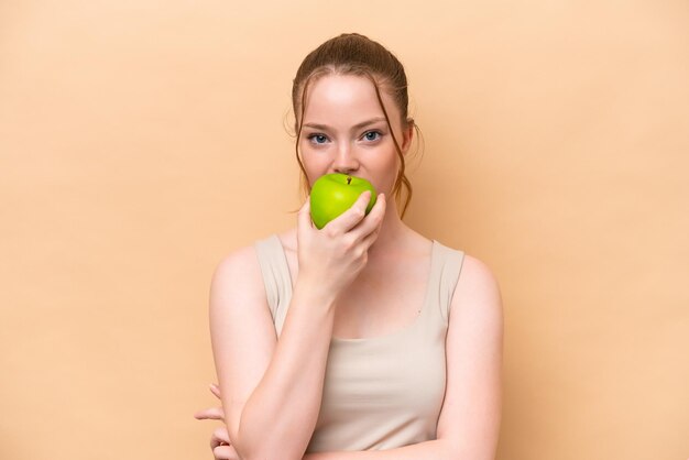 Young caucasian girl isolated on beige background eating an apple