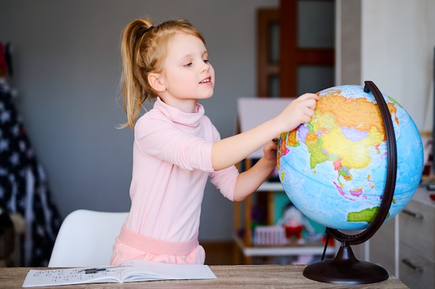 Young caucasian girl looking at earth globe at home.