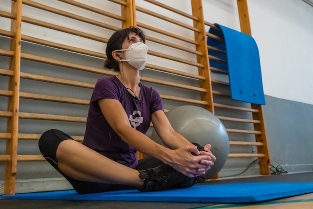 Young caucasian girl with face mask doing stretching after finishing the exercise in a gym