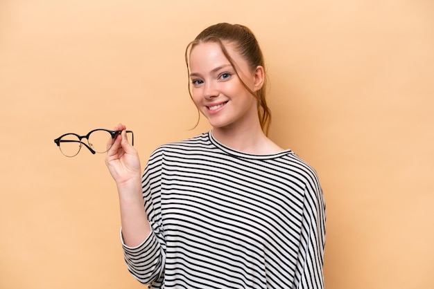 Young caucasian girl with glasses isolated on beige background smiling a lot