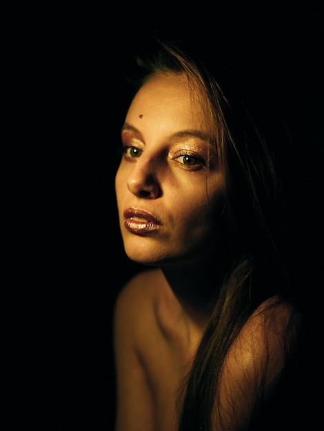 Young caucasian girl with golden make-up in the dark.