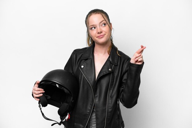 Young caucasian girl with a motorcycle helmet isolated on white background with fingers crossing and wishing the best