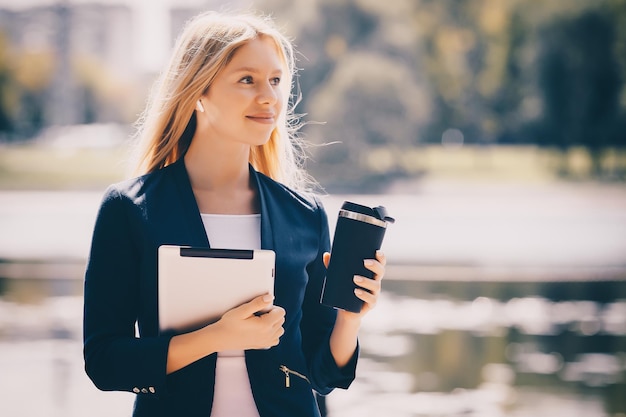 Young caucasian girl with wireless headphones in the park using tablet phone and smiling