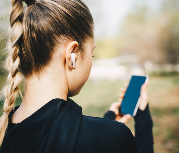 Young caucasian girl with wireless headphones in the park using tablet and smiling