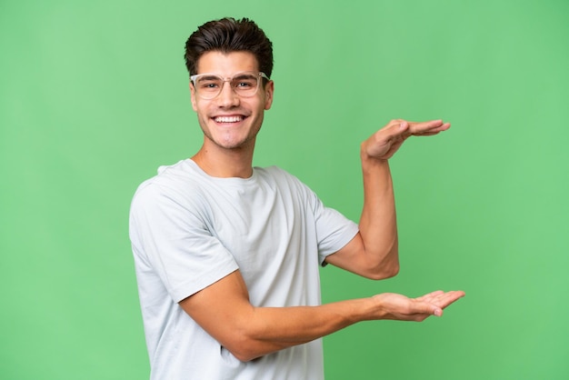 Young caucasian handsome man over isolated background holding copyspace to insert an ad