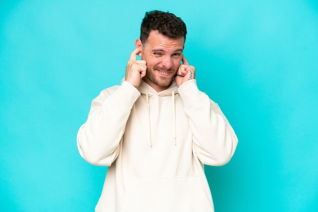 Young caucasian handsome man isolated on blue background frustrated and covering ears