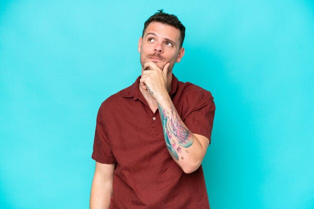 Young caucasian handsome man isolated on blue background having doubts