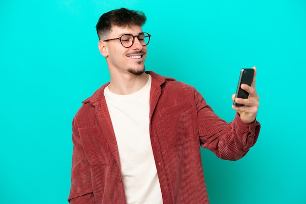 Young caucasian handsome man isolated on blue background making a selfie