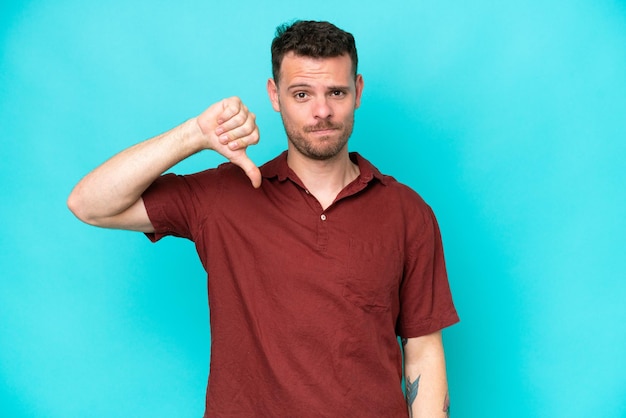 Young caucasian handsome man isolated on blue background showing thumb down with negative expression