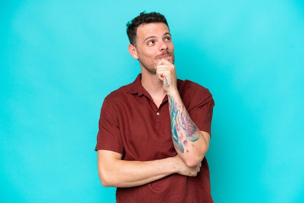 Photo young caucasian handsome man isolated on blue background thinking an idea while looking up