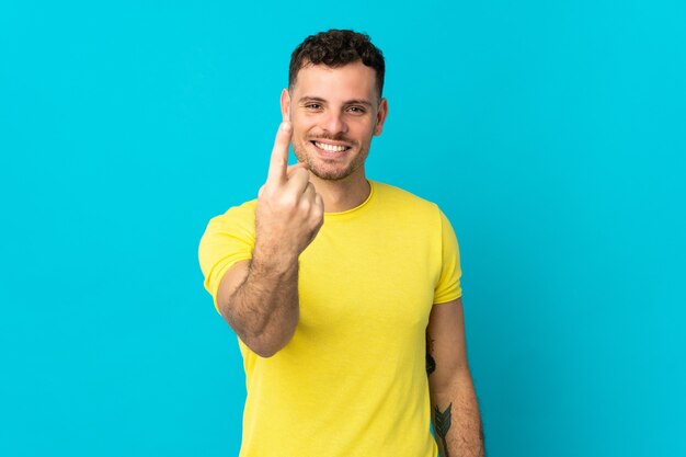 Young caucasian handsome man isolated on blue doing coming gesture