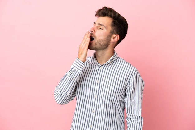 Young caucasian handsome man isolated on pink background yawning and covering wide open mouth with hand