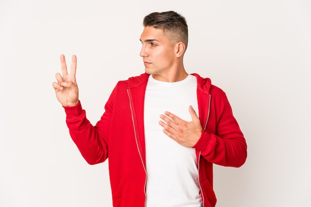 Young caucasian handsome man isolated taking an oath, putting hand on chest.