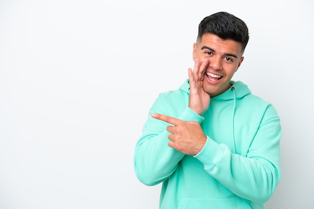 Young caucasian handsome man isolated on white background pointing to the side to present a product and whispering something