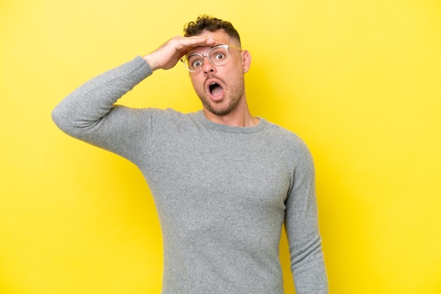 Young caucasian handsome man isolated on yellow background doing surprise gesture while looking front