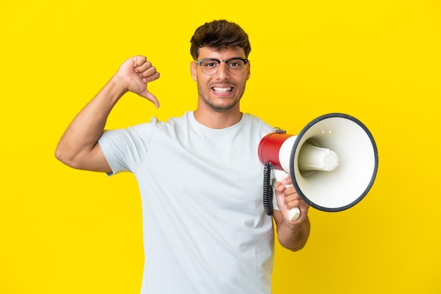 Young caucasian handsome man isolated on yellow background holding a megaphone and proud and selfsatisfied